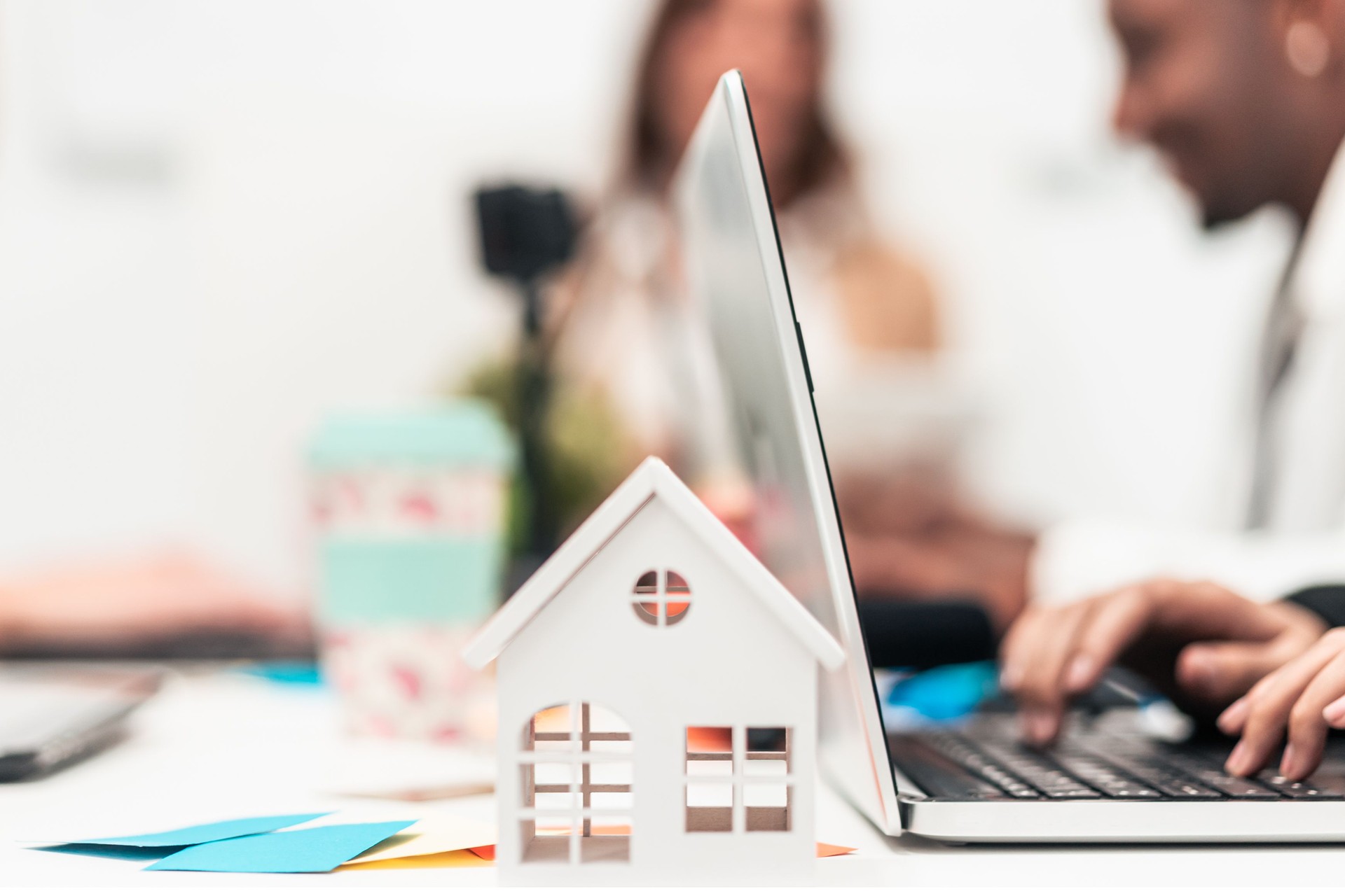 Closeup of white house and employees working with laptops in the office.  Real estate value and cost concept. Technology, mortgage, rent and buy concept.