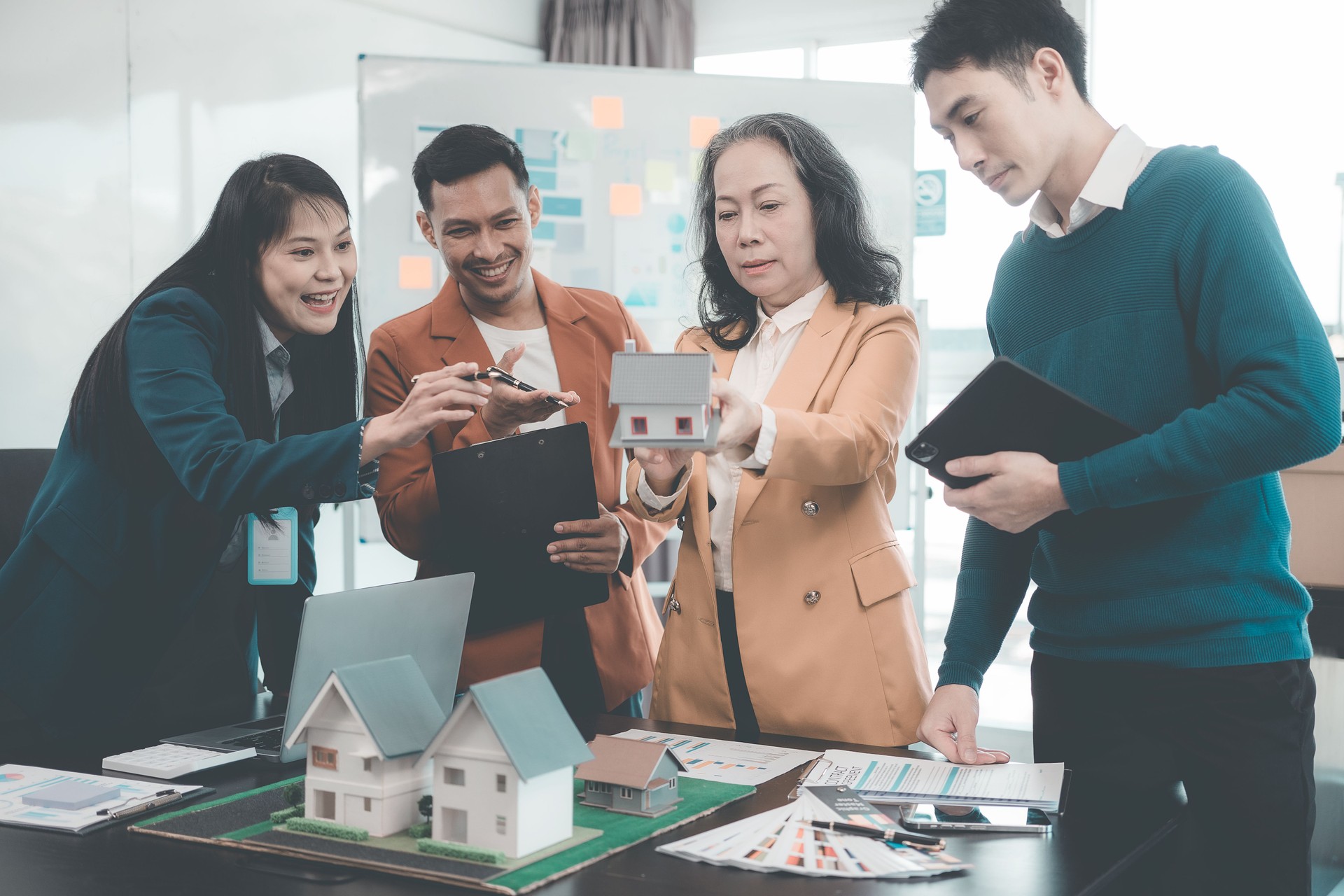 Businessmen are meeting in the office with laptops and architectural models, real estate agent presents house model to young couple and businesswoman in office
